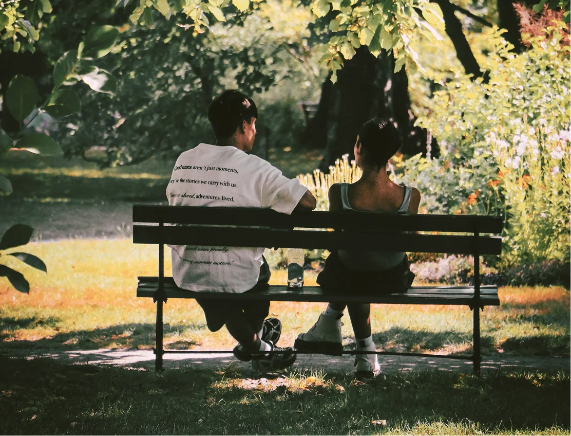 Two residents talking on a bench under dappled trees
